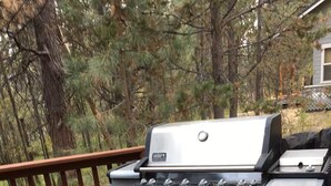 Una parrilla para barbacoa en una terraza de madera con barandilla.