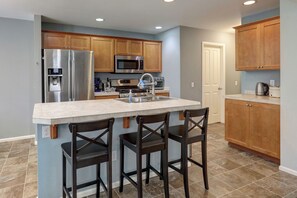 A modern kitchen with a central island, stainless steel appliances, wooden cabinets, and a tiled floor. - Peaceful Bothell Home 3B2.5B for Extended Stay (Bothell)