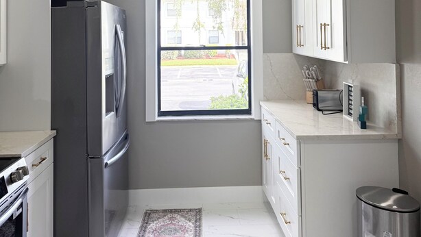 Eine moderne Küche mit einem Edelstahl-Kühlschrank, weißen Schränken, einem Fenster mit Blick und einer kleinen Mülltonne.