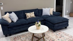 Ein Wohnzimmer mit einem dunkelblauen Modulsofa, einem weißen runden Couchtisch mit floraler Dekoration und einem Teppich mit Muster.