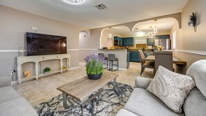 A modern living room with a flat-screen TV, a coffee table, and a sofa. There is a kitchen in the background with a dining area. - 3-bedroom house in tranquil Naples with cool AC comfort (Naples)
