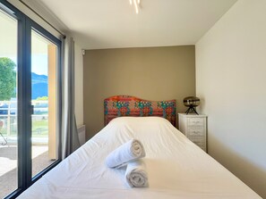 Ein Hotelzimmer mit Bett, Fenster mit Aussicht, Nachttisch mit Lampe und einem gemusterten Kopfteil.