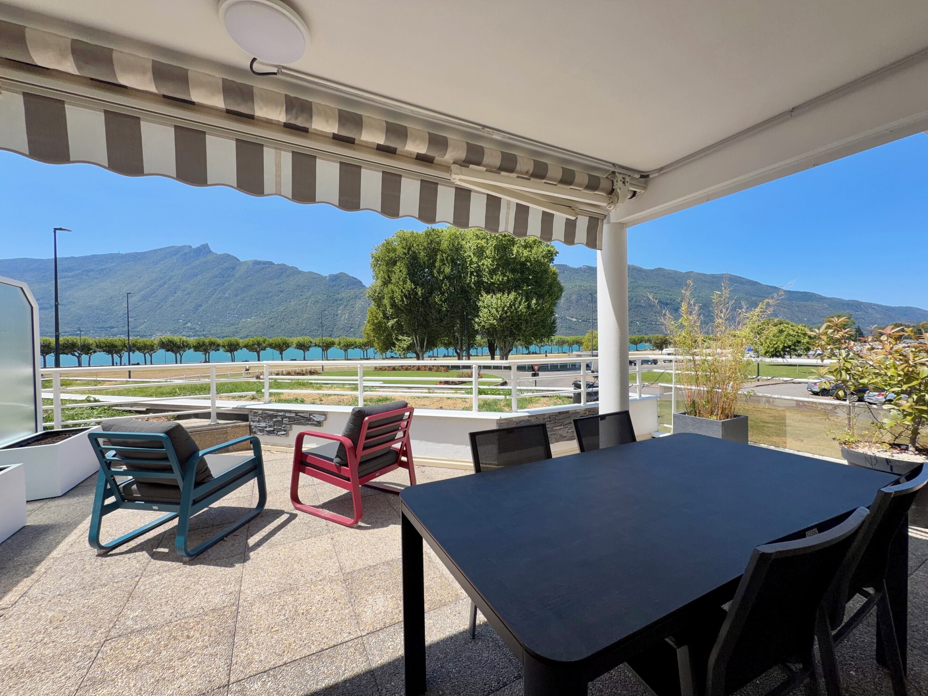 Um pátio externo com mesa e cadeiras, com vista para um lago e montanhas.