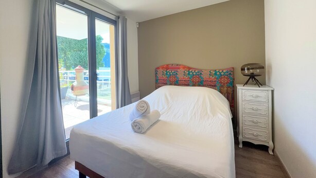 Ein Hotelzimmer mit Bett, Nachttisch, Lampe und Blick ins Freie.