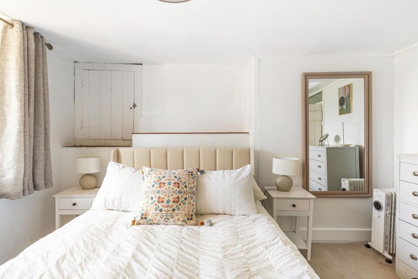 A bedroom with a bed, two bedside tables with lamps, a dresser, a mirror, and a radiator.