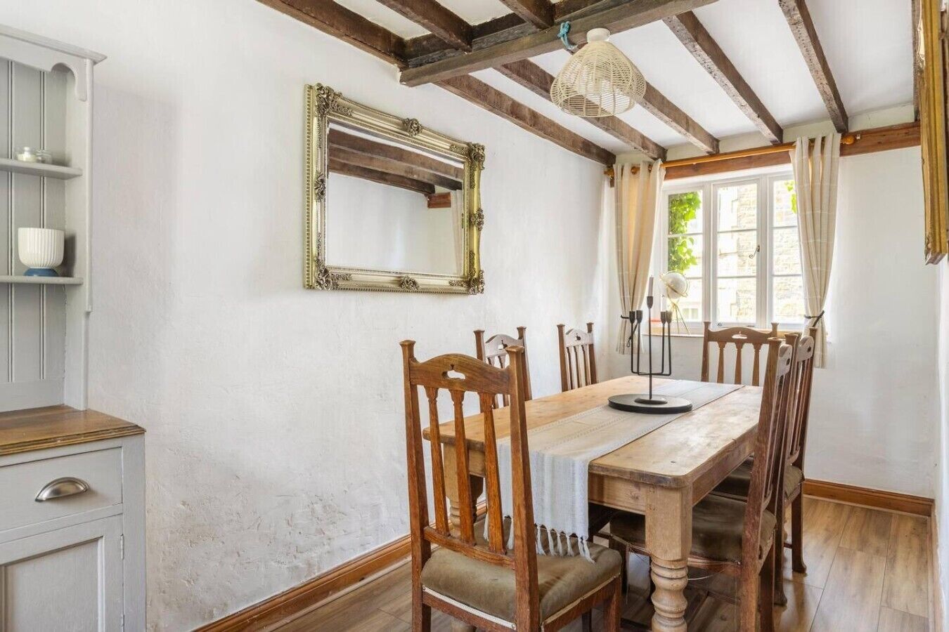 A dining room with a wooden table, six chairs, a chandelier, a mirror, and a window with curtains.