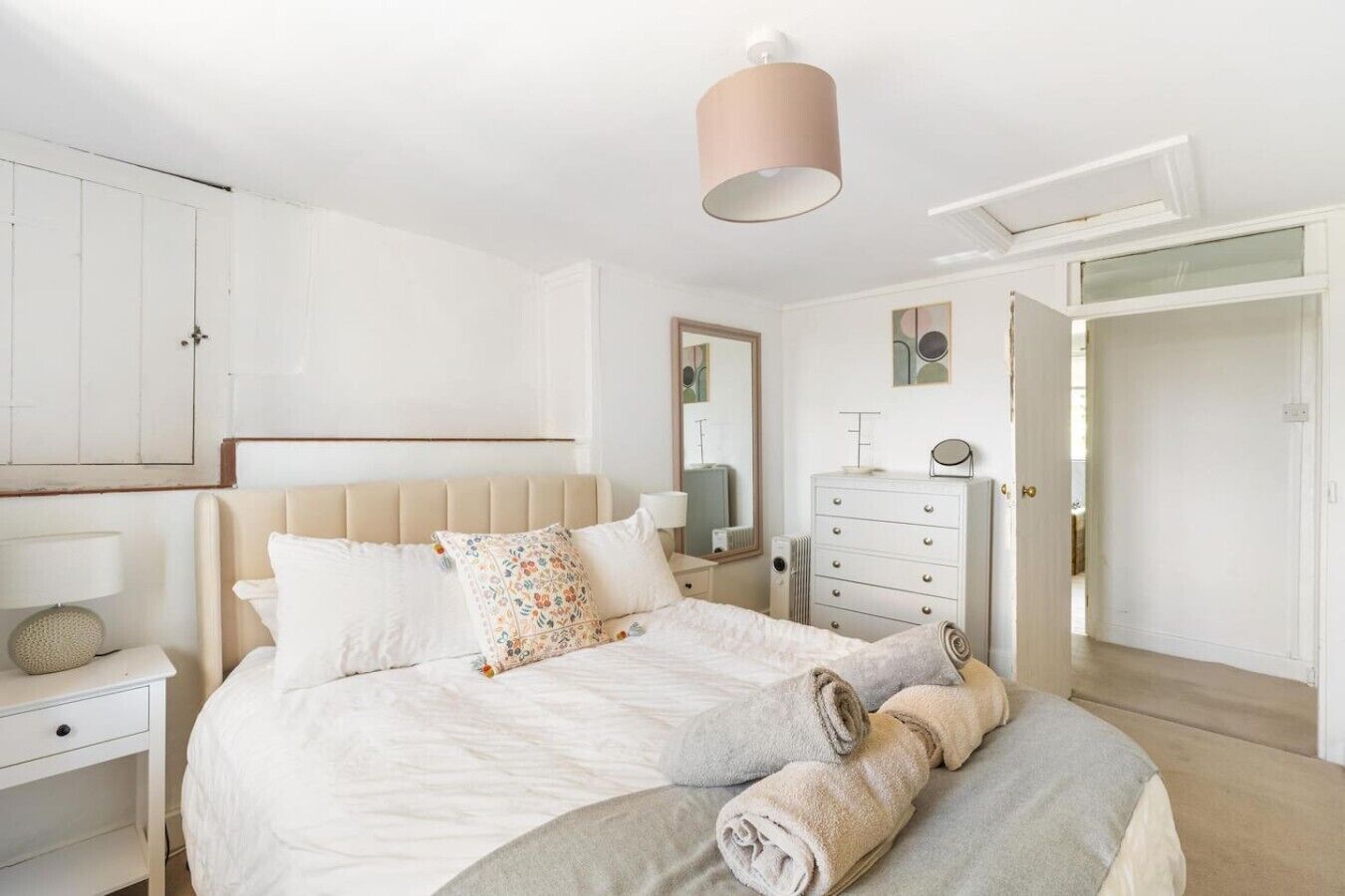 Een slaapkamer met een bed, een dressoir, een spiegel en een deur die naar een andere kamer leidt.