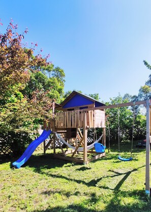 A wooden playhouse with a blue roof, a slide, and a swing set. - The House with the Blue Door – Charm and Authenticity in the Gers (Saint-Orens-Pouy-Petit)