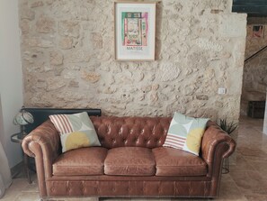 Un canapé en cuir marron avec des coussins à rayures, placé devant un mur en pierre à la texture particulière, et une œuvre d’art encadrée au-dessus.