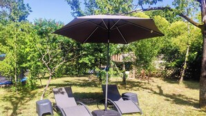 Een patio met een grote parasol, vier loungesteilen en een kleine tafel.