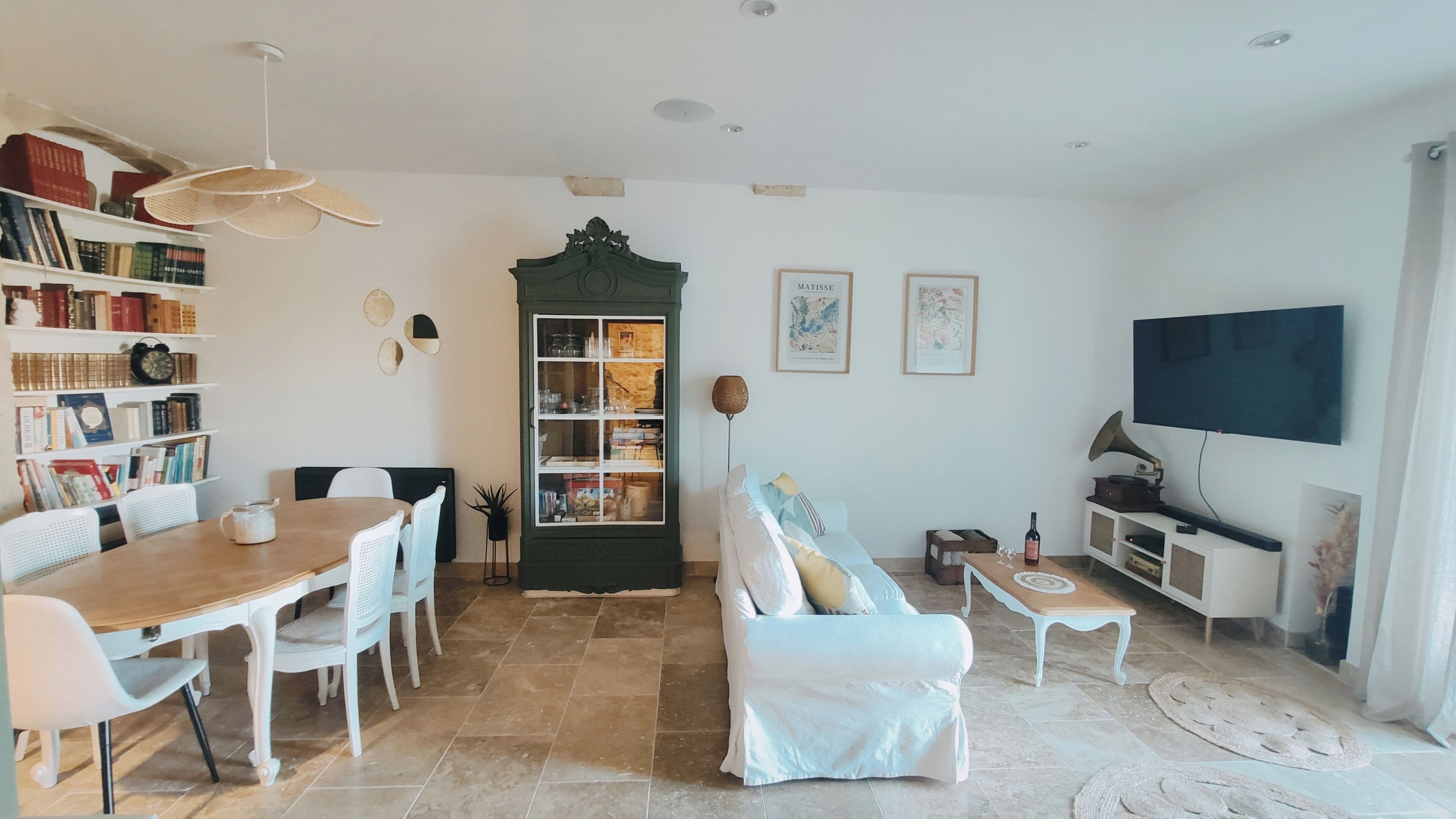 A living room with a dining table, chairs, a sofa, a bookshelf, a cabinet, a television, and a wall-mounted speaker.