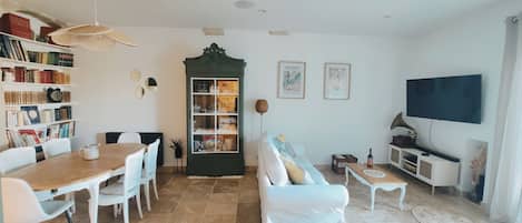 Una sala de estar con mesa de comedor, sillas, sofá, estantería, armario, televisor y altavoz de pared.