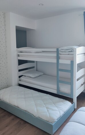 A bunk bed with a mattress and pillows, a small shelf, and a wall with a patterned curtain. - The House with the Blue Door – Charm and Authenticity in the Gers (Saint-Orens-Pouy-Petit)