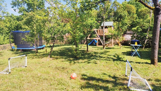 Een achtertuin met een trampoline, een speeltuintje en een glijbaan.