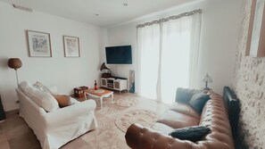 A living room with a white sofa, a brown leather couch, a small table, and a television. - The House with the Blue Door – Charm and Authenticity in the Gers (Saint-Orens-Pouy-Petit)