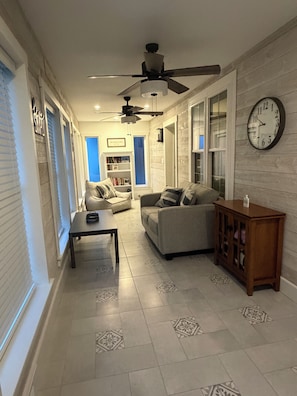 A living room with a sofa, a coffee table, a clock, and a ceiling fan.