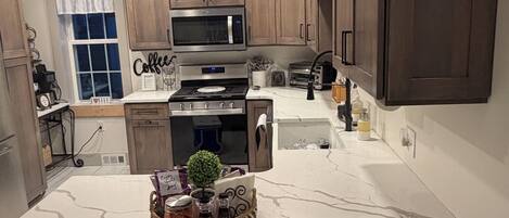 A modern kitchen with wooden cabinets, a central island, a microwave, stove, and a sink.