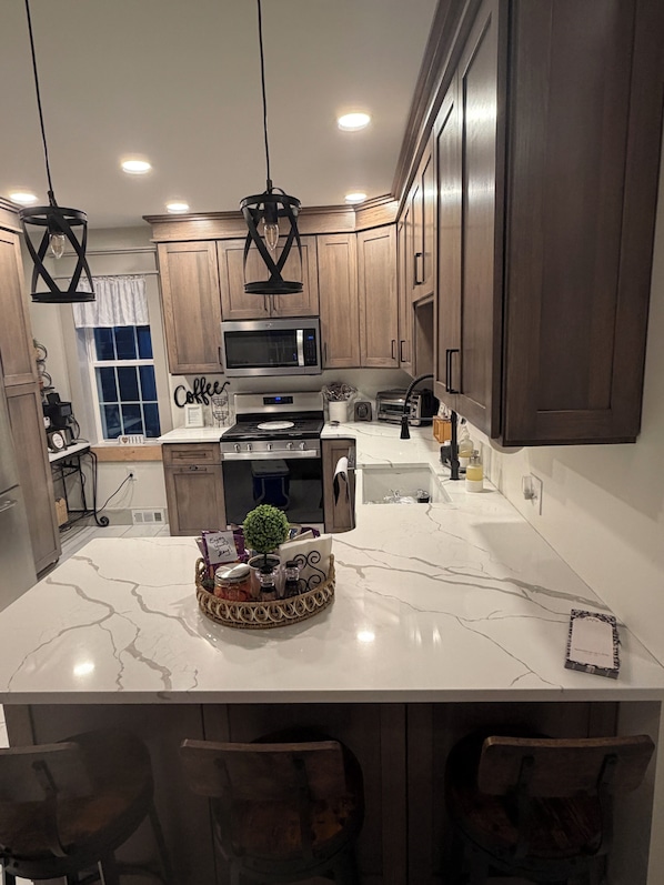 A modern kitchen with wooden cabinets, a central island, a microwave, stove, and a sink.