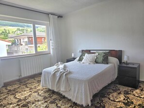 A bedroom with a bed, nightstands, a window with curtains, and a radiator. - La Coqueta Apartment 2034 (San Miguel de Meruelo)