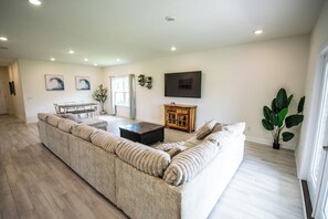 A spacious living room with a large beige sectional sofa, a wooden coffee table, and a flat-screen TV mounted on the wall. - Spacious Gulf Breeze Retreat: Near Pensacola & Navarre Beaches & Dining (Gulf Breeze)