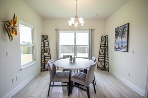 A dining area with a round table, four chairs, a chandelier, and two decorative shelves. - Spacious Gulf Breeze Retreat: Near Pensacola & Navarre Beaches & Dining (Gulf Breeze)