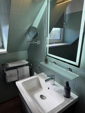 Een moderne badkamer met een grote spiegel, een witte wastafel en een handdoekrek met handdoeken.