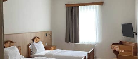 Una habitación de hotel con dos camas de madera, un escritorio, una silla, un televisor y una ventana con cortinas.