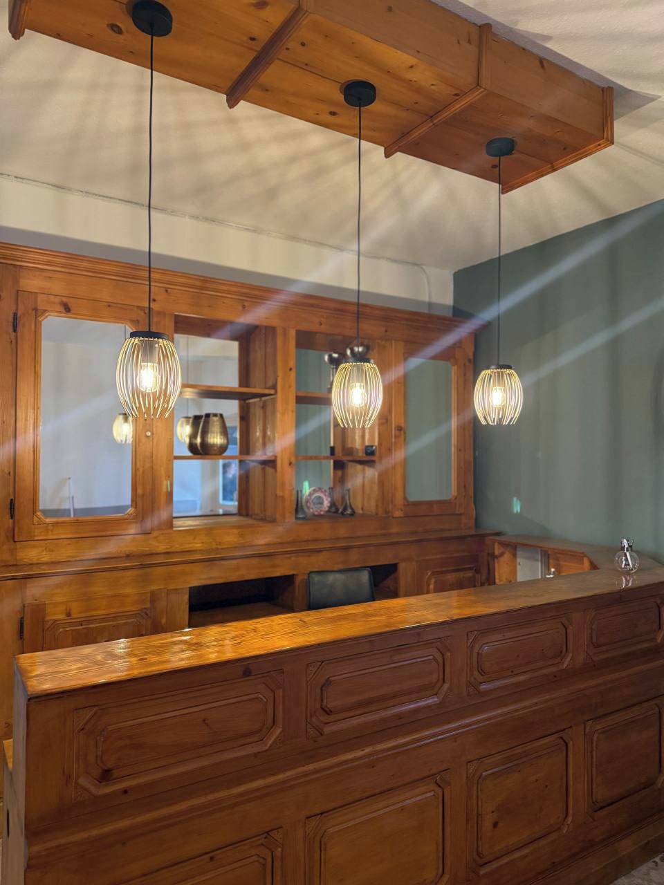 Un armario de madera con puertas de cristal, un banco de madera y lámparas colgantes.