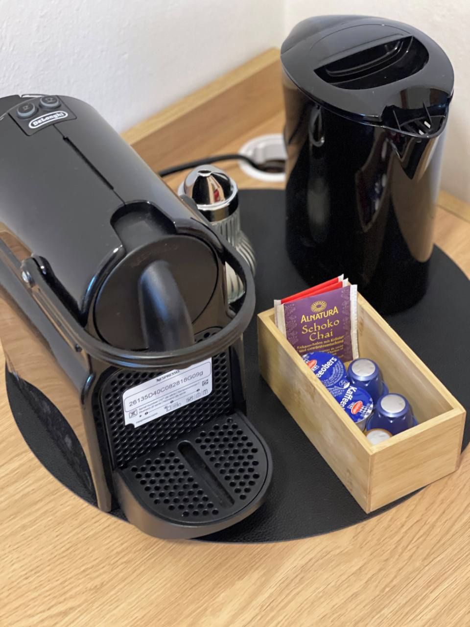 A coffee maker and a box of AlnaturSchoko Chai tea bags on a wooden tray.
