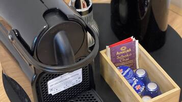 A coffee maker and a box of AlnaturSchoko Chai tea bags on a wooden tray.