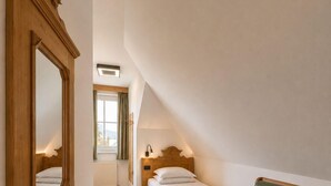 A room with a wooden bed, a green leather chair, a wooden nightstand, and a large mirror on the wall. - Pension Ursula (Pfaffstätten)