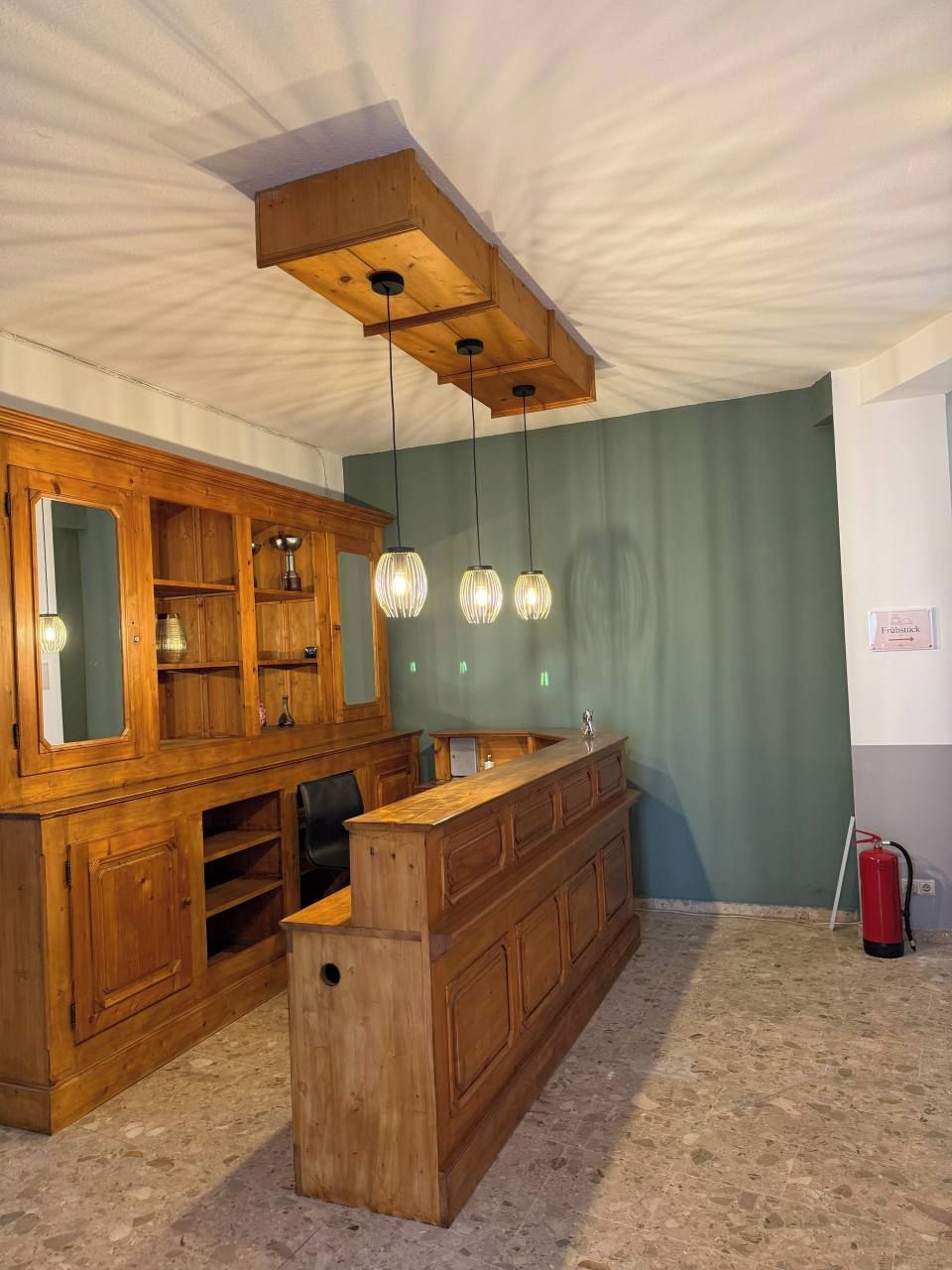 Ein Zimmer mit einer Holztresorecke, einem großen Spiegelkorpus und Pendelleuchten.