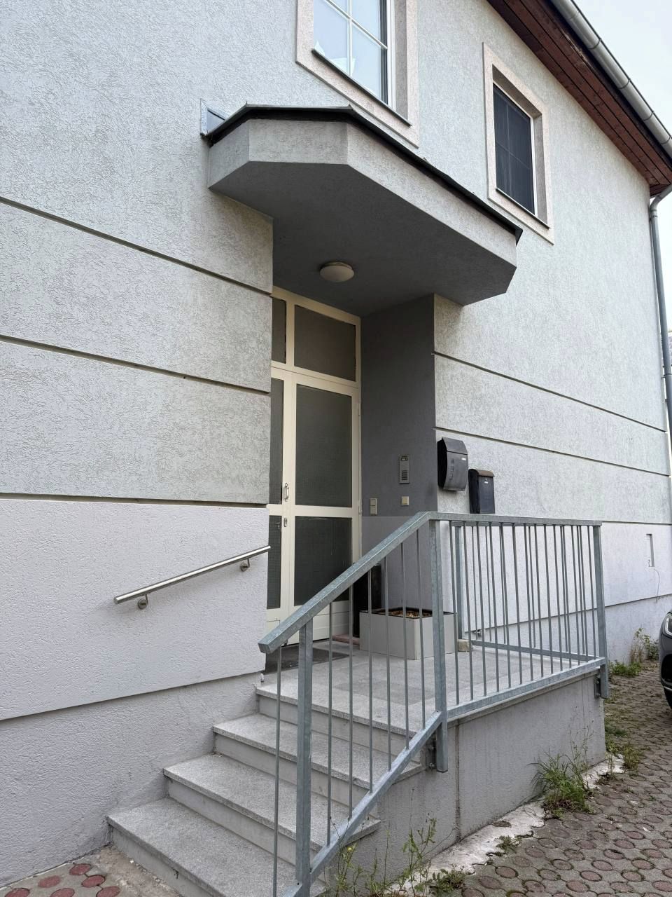 Un edificio de fachada de concreto, con una escalera que conduce a una puerta y un pequeño balcón con barandilla de metal.