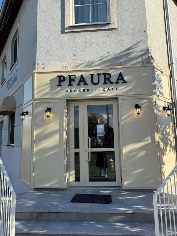 A building facade with a sign reading 'PFAURA BÄCKERI CAFE' and a visible entrance with steps leading up to it. - Pension Ursula (Pfaffstätten)