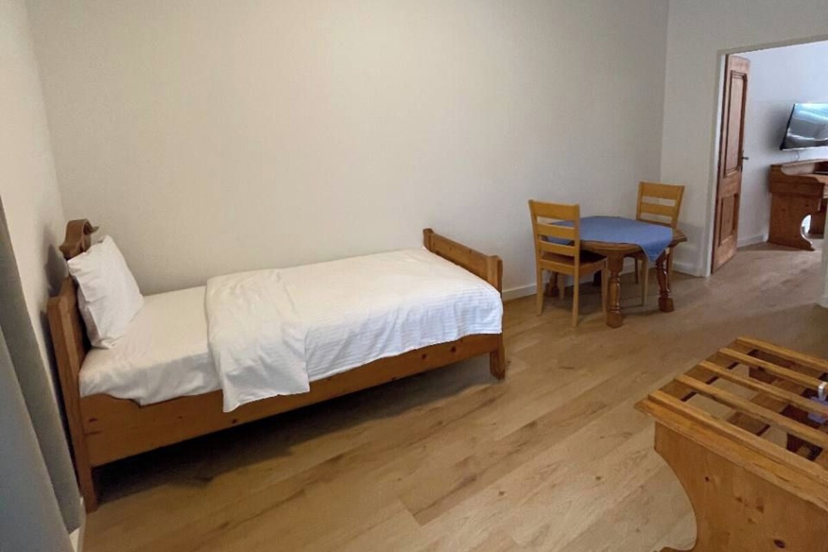 Een kamer met een enkel bed, een houten stoel, een klein tafeltje en een televisie.