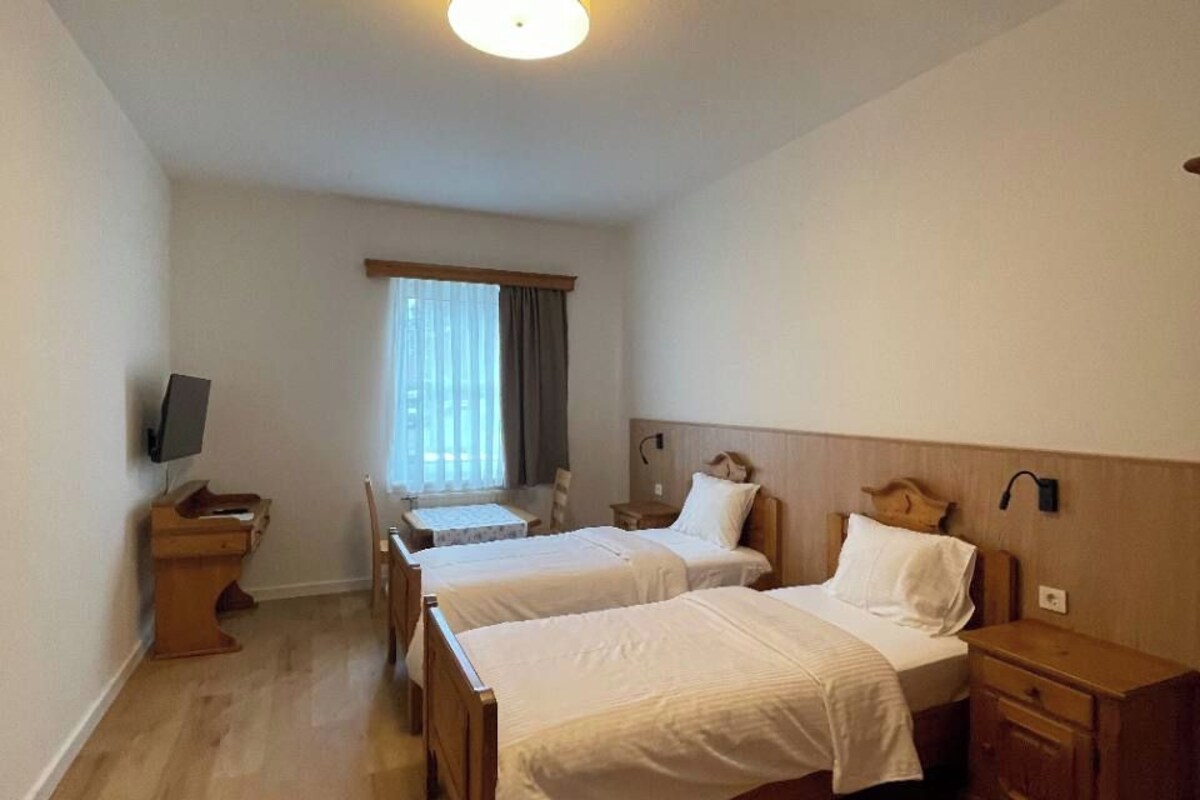 Een hotelkamer met twee enkele bedden, een bureau met stoel, een televisie en een raam met gordijnen.