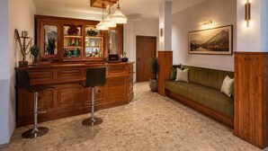 A hotel lobby with a wooden reception desk, two bar stools, a green sofa, and a framed landscape painting on the wall. - Pension Ursula (Pfaffstätten)