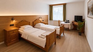 A hotel room with two wooden beds, a desk with a chair, a television, and a window with curtains. - Pension Ursula (Pfaffstätten)