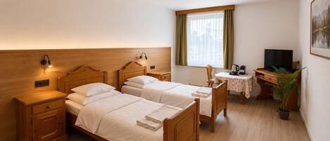 Habitación de hotel con dos camas de madera, un escritorio con silla, televisión y ventana con cortinas.
