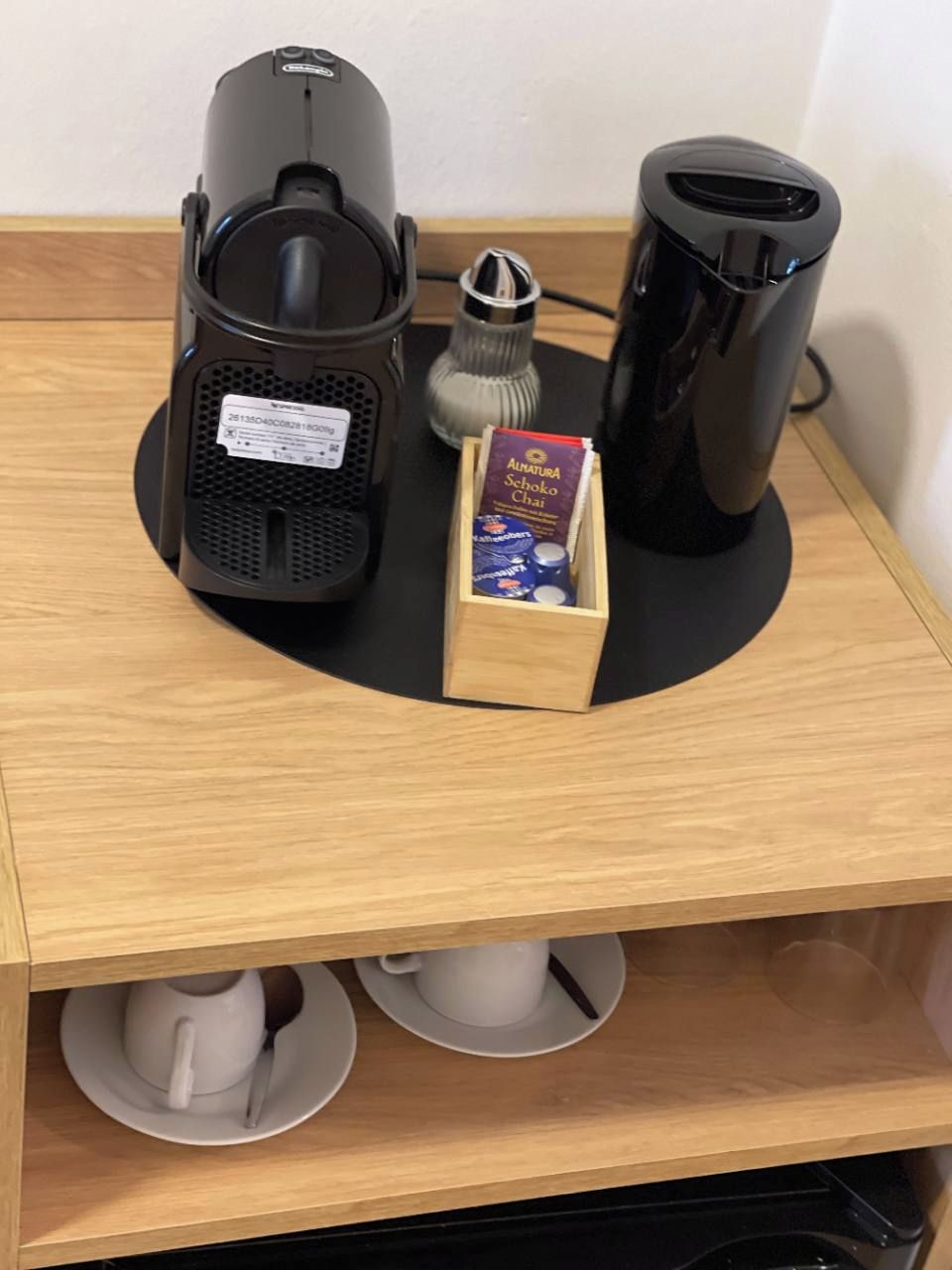A coffee machine, a tea infuser, and a box of tea bags on a wooden surface.