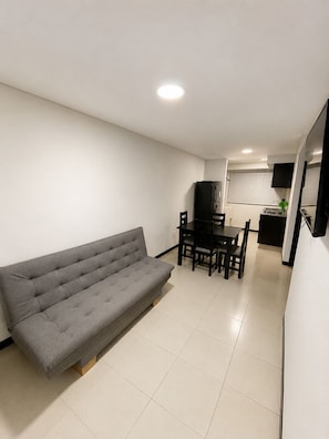 A compact living space with a sofa, dining table, chairs, a kitchen area with a stove, and a TV mounted on the wall. - Modern apartment near Parque del Café (Montenegro)