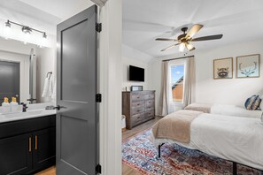Ein Schlafzimmer mit einem Bett, einem Deckenventilator, einem Schminktisch, einem Fernseher und einem Fenster mit Vorhängen.
