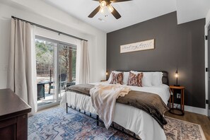 A bedroom with a large bed, a ceiling fan, a view through the window, and a sign on the wall. - BRAND NEW! Tall Timbers Modern Cabin w/ Hot Tub (Hollister)