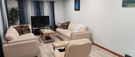 A living room with a sofa, armchair, coffee table, TV, and a plant.