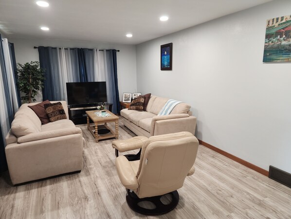 A living room with a sofa, armchair, coffee table, TV, and a plant.