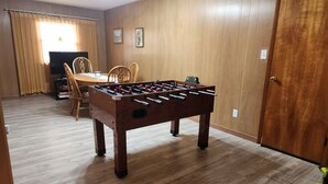 Una stanza con pavimento in legno, una porta in legno, un tavolo in legno con sedie e un tavolo da calcio.