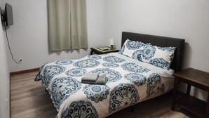 A bedroom with a bed, a nightstand, a lamp, and a TV mounted on the wall.