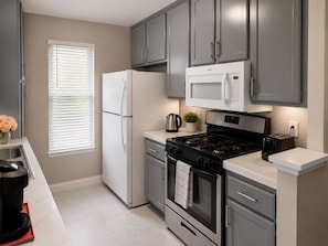 A modern kitchen with grey cabinets, a white refrigerator, a stove, and a microwave. - Modern 2BR Condo Near the Las Vegas Strip (Las Vegas)