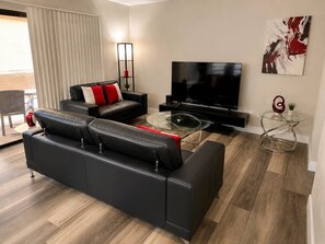 A modern living room with a black leather sofa, a glass coffee table, a flat-screen TV, and a minimalist decor. - Modern 2BR Condo Near the Las Vegas Strip (Las Vegas)
