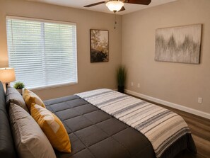 Een slaapkamer met een bed, een plafondventilator, een raam met jaloezieën en twee aan de muur hangende schilderijen.